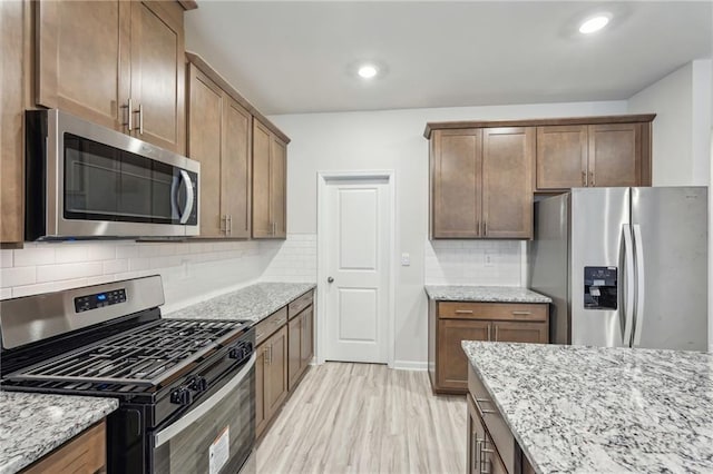 kitchen featuring backsplash, stainless steel appliances, light stone counters, and light hardwood / wood-style floors