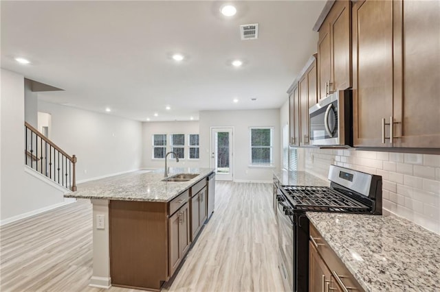 kitchen with sink, light stone counters, backsplash, an island with sink, and appliances with stainless steel finishes