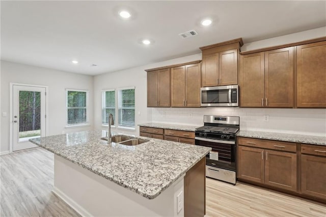 kitchen with light stone countertops, sink, appliances with stainless steel finishes, and an island with sink