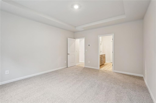 unfurnished bedroom with a raised ceiling, connected bathroom, and light carpet