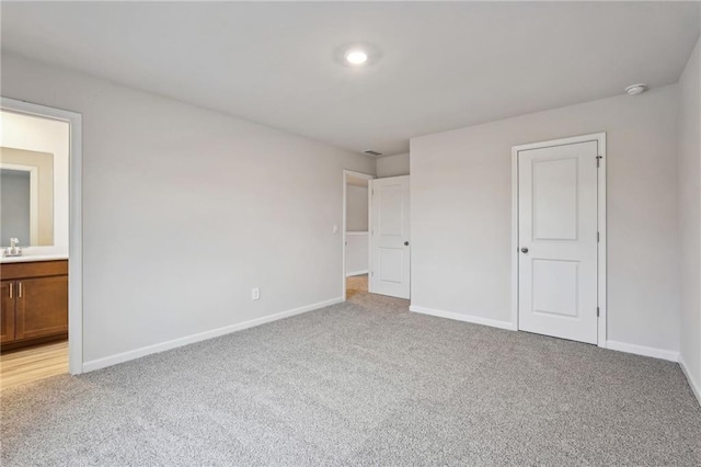 unfurnished bedroom featuring ensuite bathroom, light colored carpet, and sink