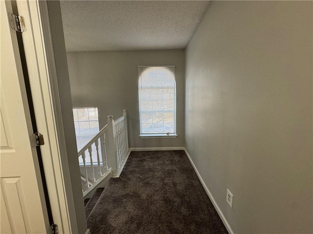 hallway featuring dark carpet and a textured ceiling