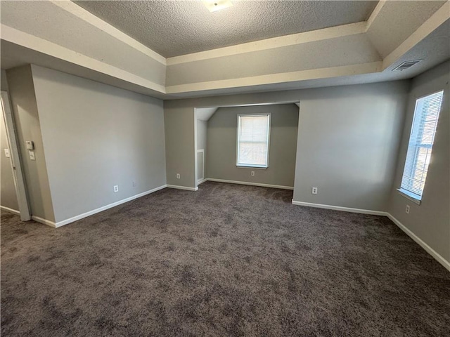 spare room featuring a textured ceiling, a tray ceiling, and dark carpet