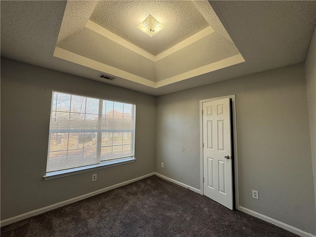 unfurnished room featuring a textured ceiling, a tray ceiling, and dark carpet