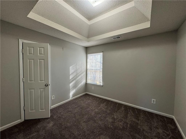 spare room with dark colored carpet, a raised ceiling, and a textured ceiling