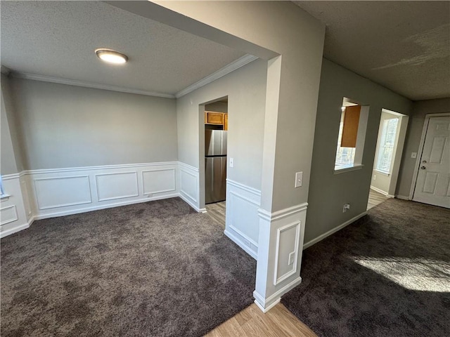 spare room with dark colored carpet, a textured ceiling, and crown molding