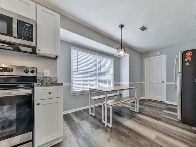 kitchen with white cabinetry, hanging light fixtures, stainless steel appliances, dark hardwood / wood-style floors, and dark stone counters