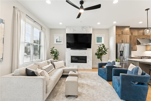 living room with a high end fireplace, light hardwood / wood-style floors, and ceiling fan