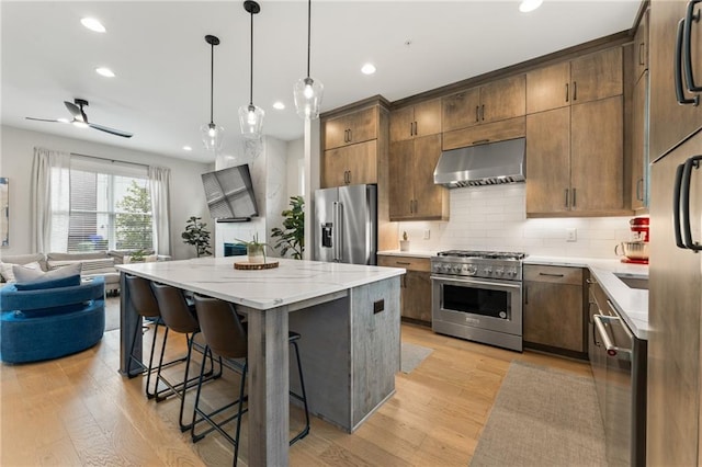 kitchen featuring ventilation hood, a breakfast bar area, high end appliances, a center island, and light hardwood / wood-style flooring