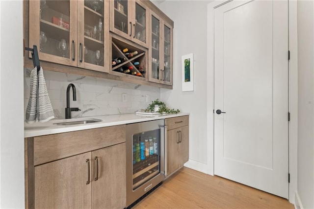 bar with tasteful backsplash, beverage cooler, light hardwood / wood-style floors, and sink