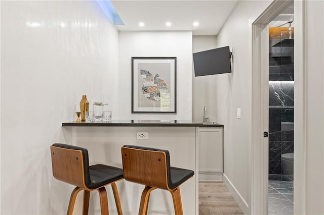 bar featuring white cabinetry, sink, light hardwood / wood-style flooring, and dark stone countertops