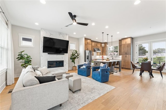 living room with ceiling fan, a high end fireplace, sink, and light hardwood / wood-style flooring