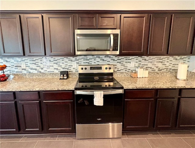 kitchen with dark brown cabinetry, light stone countertops, light tile patterned floors, appliances with stainless steel finishes, and backsplash
