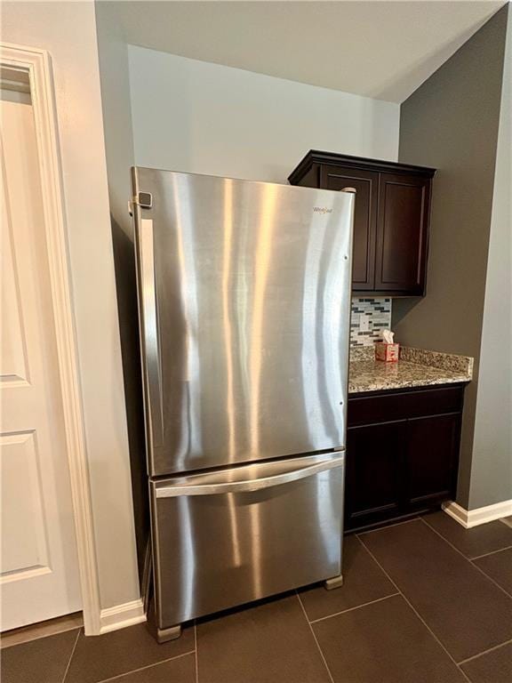 kitchen featuring dark brown cabinets, light stone countertops, freestanding refrigerator, baseboards, and dark tile patterned flooring