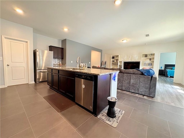 kitchen featuring dark brown cabinets, light stone counters, a sink, stainless steel appliances, and dark tile patterned flooring