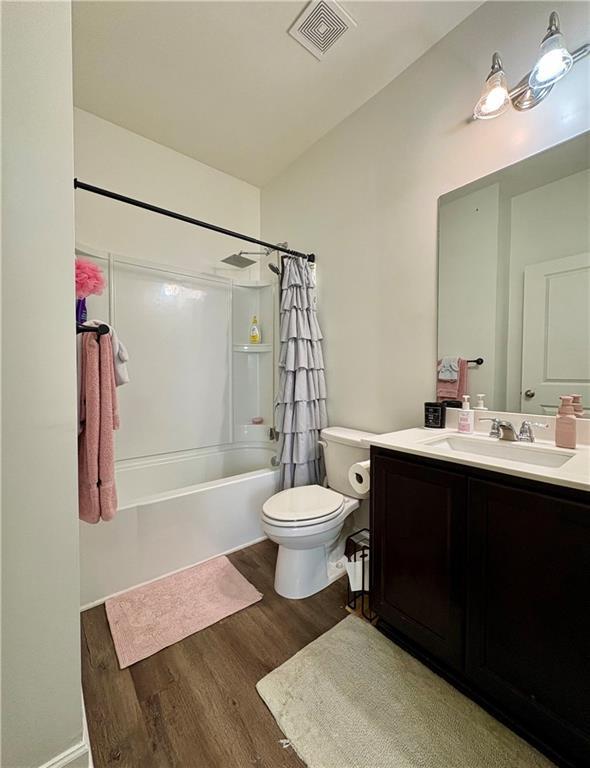 bathroom with visible vents, vanity, wood finished floors, shower / bath combination with curtain, and toilet