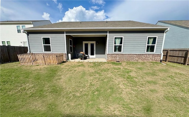 rear view of property with brick siding, a fenced backyard, french doors, and a yard