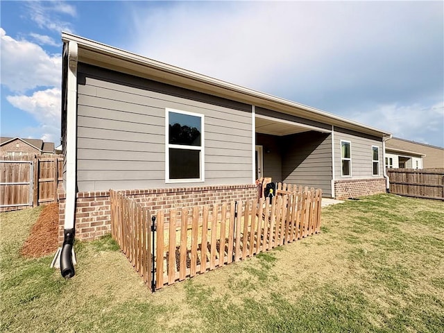 rear view of house featuring a fenced backyard, a yard, and brick siding