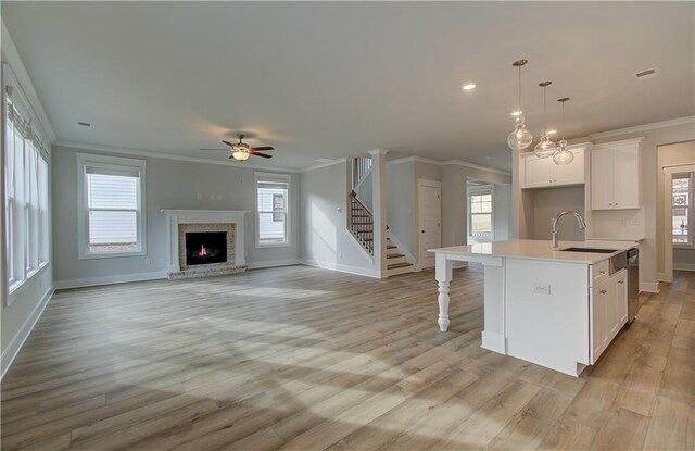 kitchen featuring white cabinets, crown molding, hanging light fixtures, ceiling fan, and an island with sink