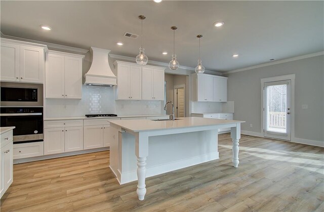 kitchen featuring built in microwave, an island with sink, oven, pendant lighting, and custom range hood