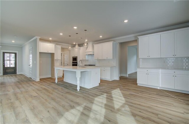 kitchen featuring a kitchen island with sink, sink, white cabinets, and hanging light fixtures