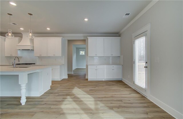 kitchen featuring custom range hood, white cabinetry, ornamental molding, and pendant lighting