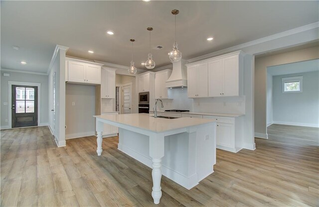 kitchen featuring hanging light fixtures, white cabinetry, premium range hood, and a kitchen island with sink