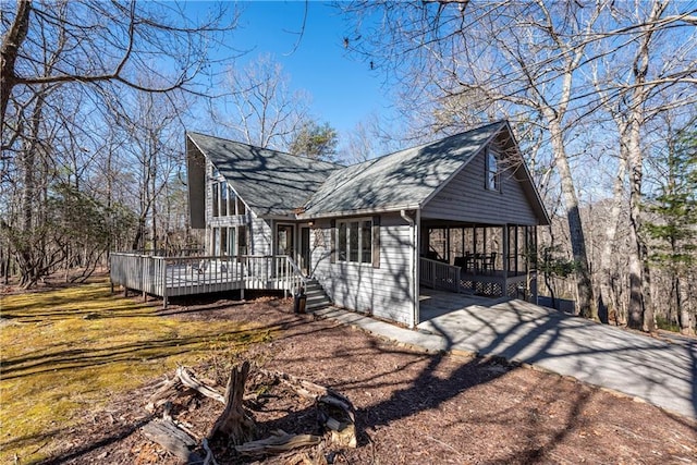 view of side of property with a carport, roof with shingles, a deck, and driveway