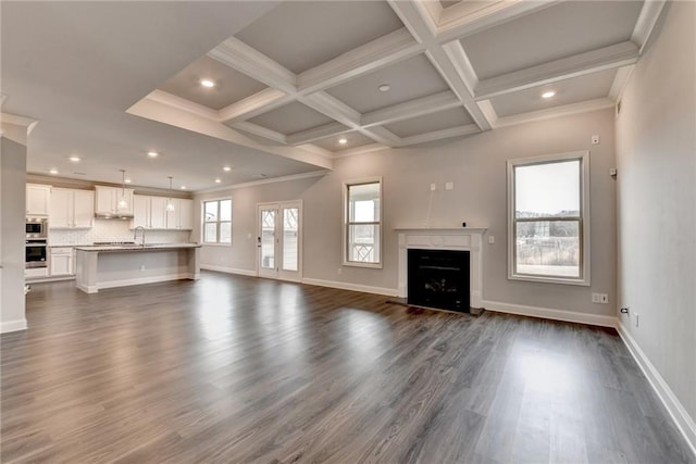 unfurnished living room with sink, coffered ceiling, a wealth of natural light, dark hardwood / wood-style flooring, and beamed ceiling