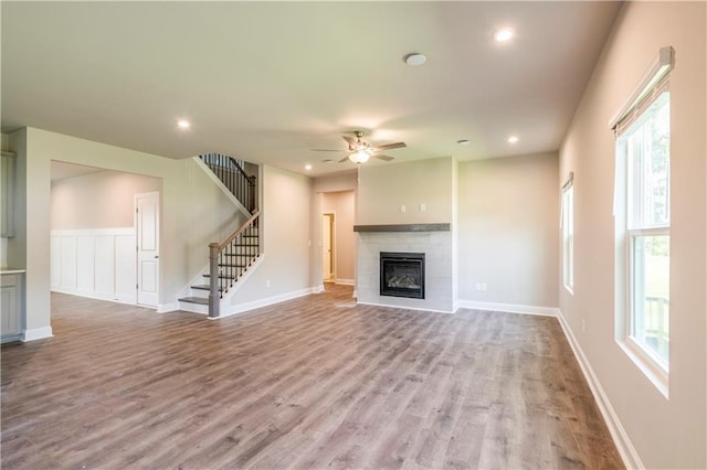 unfurnished living room featuring plenty of natural light, hardwood / wood-style flooring, a tiled fireplace, and ceiling fan