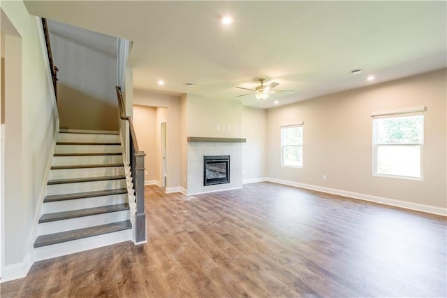 unfurnished living room featuring ceiling fan, a tiled fireplace, and hardwood / wood-style flooring