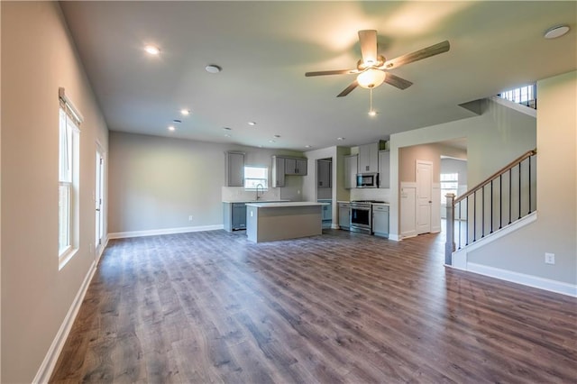 unfurnished living room featuring a wealth of natural light, ceiling fan, and dark hardwood / wood-style floors