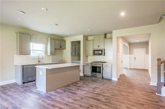 kitchen with a center island, stainless steel appliances, sink, gray cabinets, and light wood-type flooring