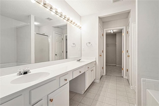 full bath with visible vents, a sink, a shower stall, and a textured ceiling