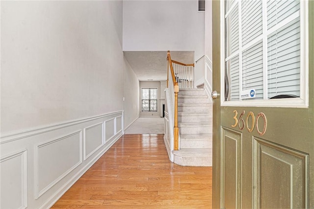 hallway with stairs, a decorative wall, light wood-style flooring, and a wainscoted wall