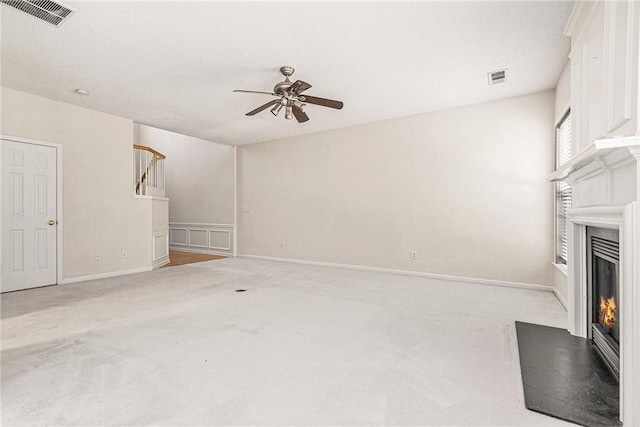 unfurnished living room with visible vents, light colored carpet, a warm lit fireplace, and ceiling fan