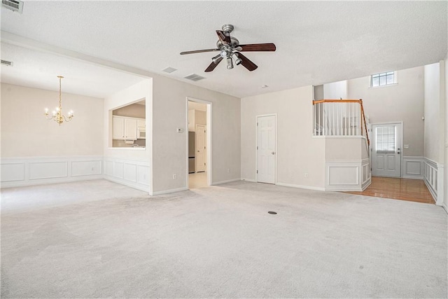 unfurnished living room with light carpet, visible vents, ceiling fan with notable chandelier, and a decorative wall