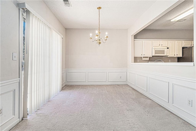 empty room featuring a textured ceiling, a chandelier, a decorative wall, light carpet, and visible vents