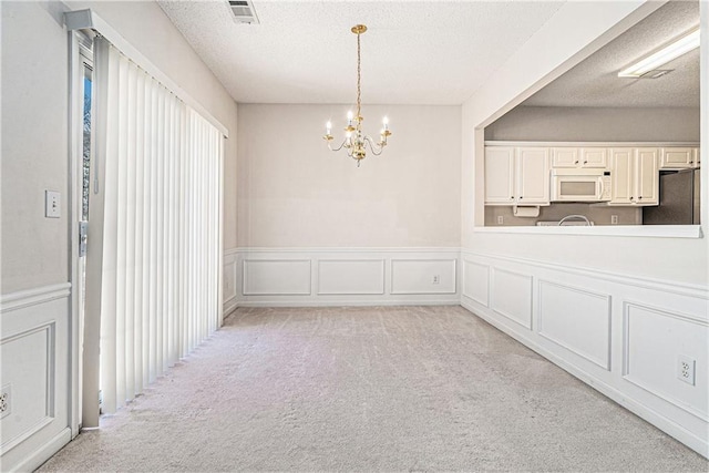 unfurnished dining area with visible vents, light carpet, a textured ceiling, a decorative wall, and a chandelier