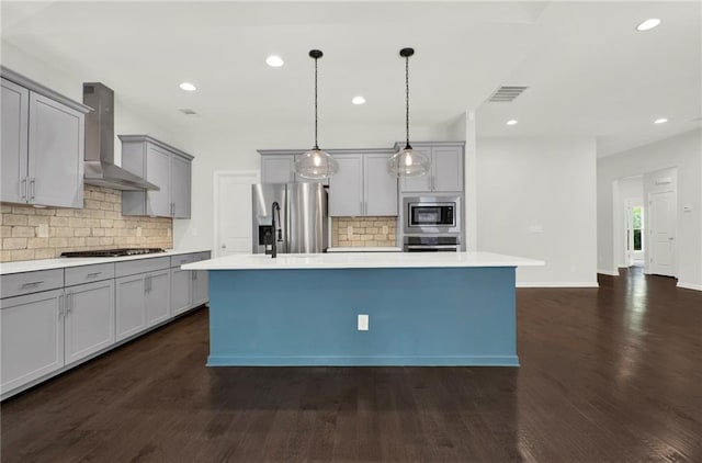 kitchen with visible vents, backsplash, gray cabinetry, wall chimney range hood, and appliances with stainless steel finishes