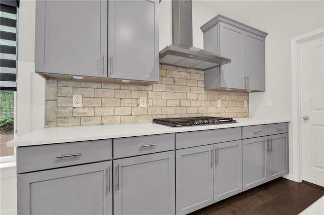 kitchen with stainless steel gas cooktop, backsplash, gray cabinetry, wall chimney range hood, and light countertops