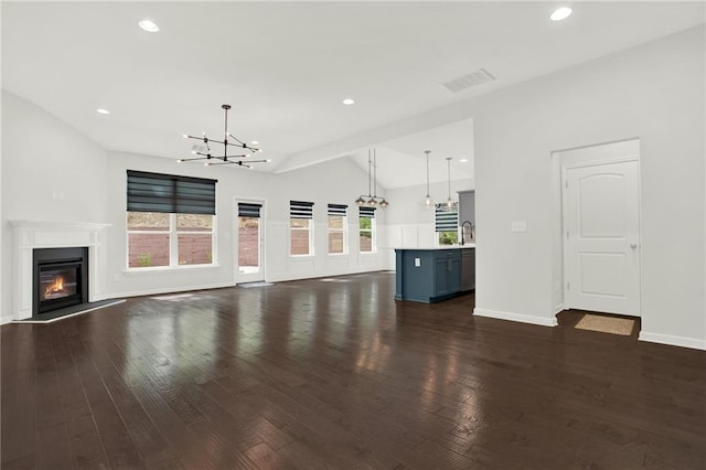 unfurnished living room with lofted ceiling, an inviting chandelier, visible vents, a glass covered fireplace, and dark wood-style flooring