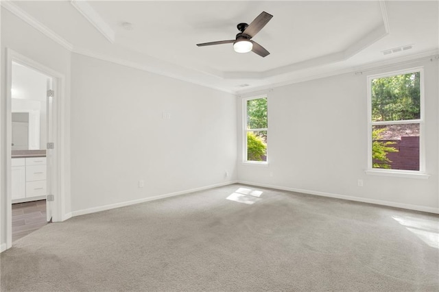 spare room with ceiling fan, light carpet, a tray ceiling, baseboards, and visible vents