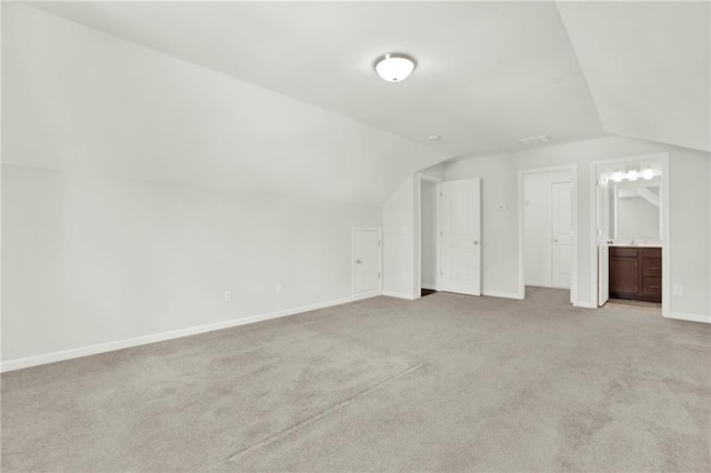 unfurnished bedroom featuring baseboards, lofted ceiling, light colored carpet, and connected bathroom
