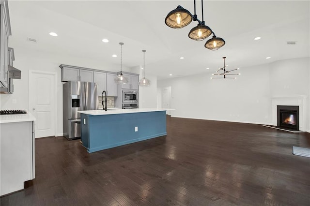 kitchen featuring an island with sink, dark wood-style floors, light countertops, appliances with stainless steel finishes, and open floor plan
