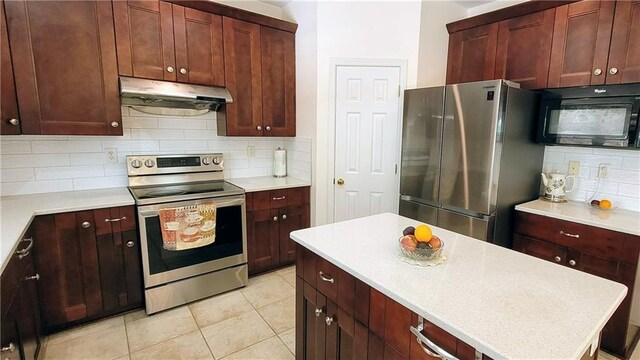 kitchen featuring light tile patterned floors, a center island, stainless steel appliances, under cabinet range hood, and backsplash