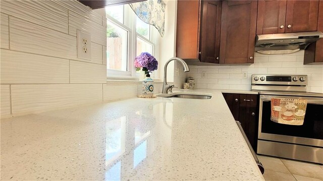 kitchen with under cabinet range hood, a sink, decorative backsplash, light stone countertops, and stainless steel range with electric stovetop