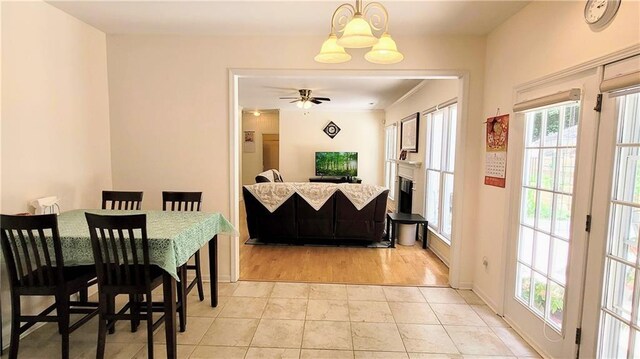 dining area featuring ceiling fan with notable chandelier, a fireplace, baseboards, and light tile patterned floors