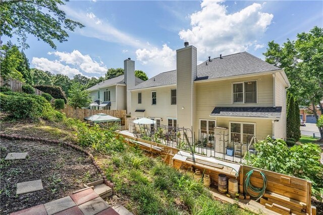 rear view of property featuring a shingled roof, a chimney, and fence