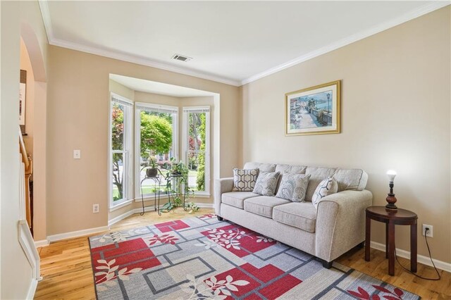 living room with baseboards, wood finished floors, visible vents, and crown molding